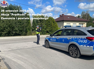 policjant stoi na poboczu drogi i mierzy prędkość, obok niego stoi radiowóz