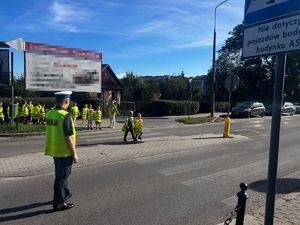 grupa dzieci ćwiczy przechodzenie przez jezdnię z policjantem