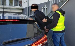 policjant w kamizelce odblaskowej prowadzi zatrzymanego