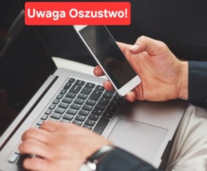 smartfon w ręku przy laptopie. Napis Uwaga oszustwo