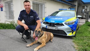 policjant pozuje ze swoim psem na tle radiowozu