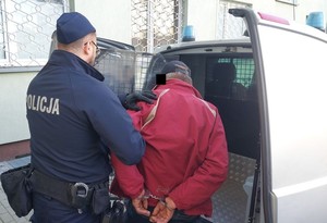 policjant prowadzi do radiowozu zatrzymanego mężczyznę