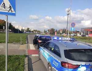 samochód osobowy i oznakowany radiowóz na jezdni, obok na ścieżce rowerowej stoi hulajnoga.