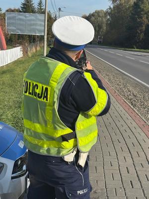 Policjant z ręcznym miernikiem prędkości na drodze prowadzi pomiar prędkości jazdy kierującego pojazdem.