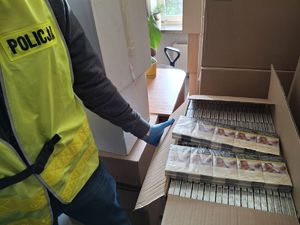 karton z paczkami papierosów, obok stoi policjant w kamizelce odblaskowej