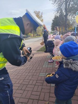 Policjant z miernikiem prędkości w reku pokazuje dziecku zapis prędkości jazdy kierującego pojazdem.