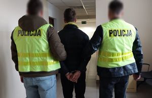 Policjanci prowadzą korytarzem komendy zatrzymanego mężczyznę.