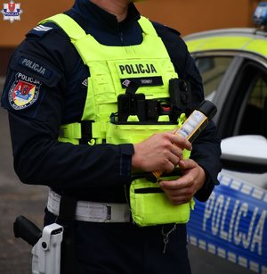 policjant w żółtej kamizelce, trzyma w rękach urządzenie do pomiaru stanu trzeźwości