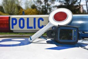 Dach radiowozu z belką świetlna, na który położona jest tarcza do zatrzymywania pojazdów oraz ręczny miernik prędkości.