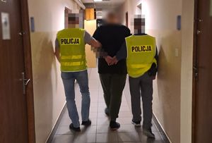 dwóch policjantów w żółtych kamizelkach prowadzi zatrzymanego mężczyznę