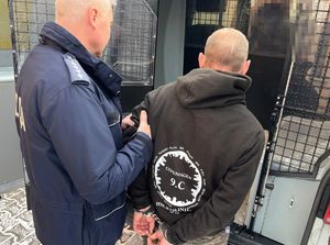 policjant prowadzi do radiowozu  zatrzymanego mężczyznę