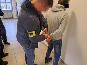 Policjant nieumundurowany z opaską z napisem policja zakłada kajdanki zatrzymanemu mężczyźnie