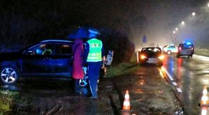zdjęcie z miejsca śmiertelnego wypadku w Turce. Policjant na miejscu zdarzenia stojący z kobietą przy samochodzie. W tle inne pojazdy.