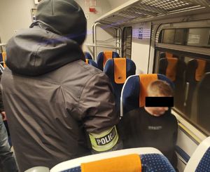 policjant stoi w pociągu. Na siedzeniu siedzi zatrzymany