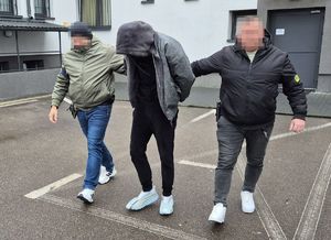 policjanci prowadzą po chodniku zatrzymanego mężczyznę