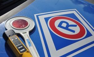 Pokrywa silnika pojazdu służbowego Policji z logo ruchu drogowego - litera R. Obok leżące urządzenie do badania stanu trzeźwości i tarcza do zatrzymywania pojazdów