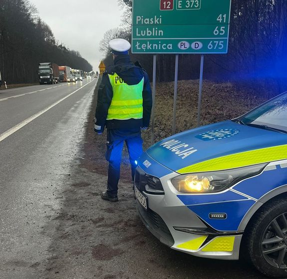 policjant przy drodze, w tle kolejka tirów
