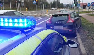 czarne volvo stojące jednym kołem na krawężniku za nim radiowóz na sygnale