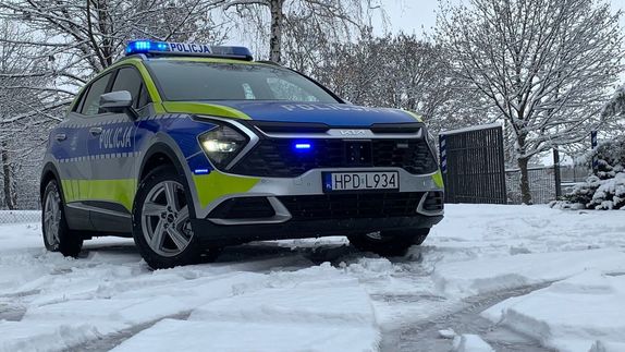 policyjny radiowóz na śniegu przy posesji z włączonymi światłami błyskowymi