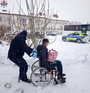 policjant pcha wózek inwalidzki z mężczyzna, w tle policyjny radiowóz