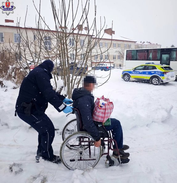 policjant pcha wózek inwalidzki z mężczyzna, w tle policyjny radiowóz