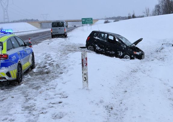 czarny samochód w zaśnieżonym rowie obok radiowóz
