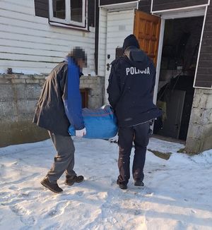 mężczyzna i policjant niosą do budynku worek z węglem