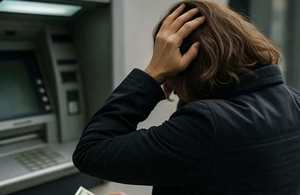 zdjęcie ilustracyjne - kobieta stoi przed bankomatem trzymając się za głowę