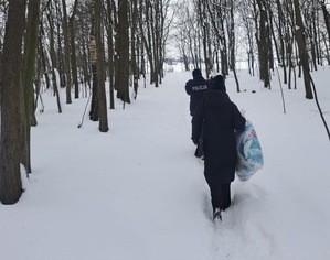 policjant z pracownicą OPS niosą rzeczy codziennego użytku droga zaśnieżoną przez las
