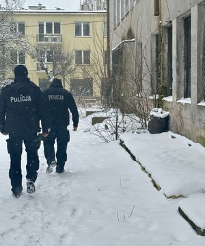 umundurowani policjanci idą po śniegu obok pustostanu