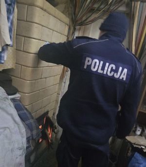 Policjant stoi przy piecu kaflowym podczas wizyty w domu mieszkańca powiatu.