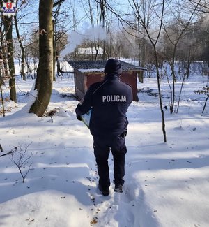 policjant idzie po śniegu wokół drzewa a przed nim mały drewniany domek