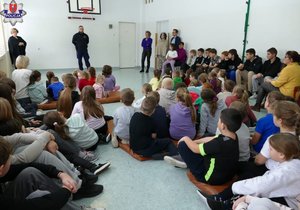 policjant stoi przed siedzącymi na podłodze dziećmi w czasie spotkania profilaktycznego