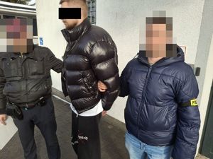 Policjanci prowadzą zatrzymanego mężczyznę.