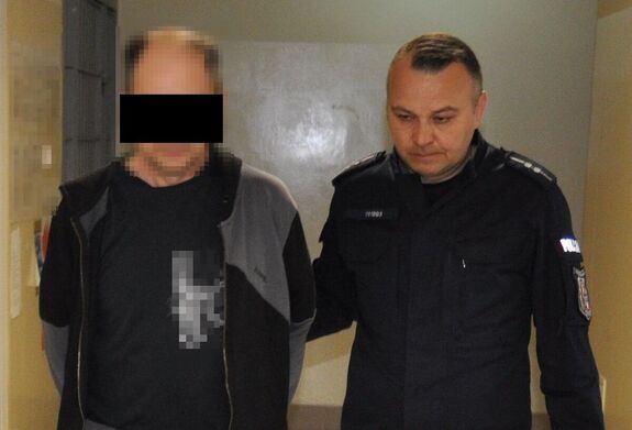 policjant prowadzi zatrzymanego 55-latka