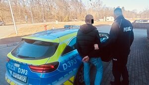 policjant i zatrzymany mężczyzna stoją przy radiowozie