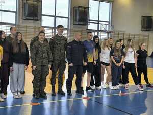 Funkcjonariusz Policji z uczniami i Wojskiem stojący w sali gimnastycznej