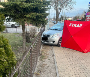 samochód marki toyota stoi przy wygiętym ogrodzeniu posesji. Obok jest rozłożony parawan z napisem straż.
