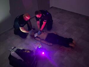 dwóch umundurowanych policjantów w pozycji siadu klęcznego ćwiczy udzielania pierwszej pomocy na fantomie