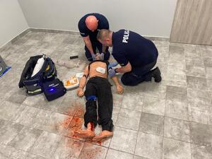 dwóch umundurowanych policjantów w pozycji siadu klęcznego ćwiczy udzielania pierwszej pomocy na fantomie