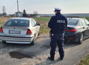 policjant stoi przy samochodzie przeprowadza interwencję, po prawej stronie znajduje się nieoznakowany radiowóz policyjny