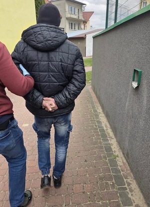 zatrzymany mężczyzna z kajdankami założonymi na ręce trzymane z tyłu idzie chodnikiem