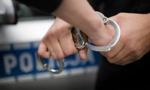 grafika przedstawiająca zakładanie kajdanek na ręce, w tle napis policja