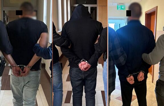 Zatrzymani mężczyźni stoją tyłem, mają na rękach trzymanych z tyłu nałożone kajdanki