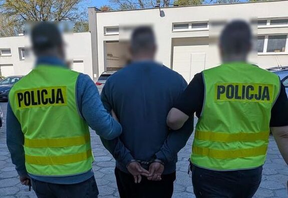 policjanci prowadzą zatrzymanego poszukiwanego