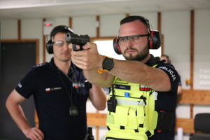 policjant oddaje strzał na strzelnicy. obok instruktor