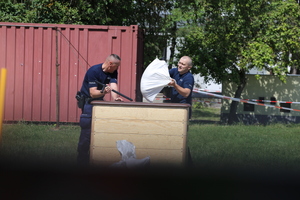 Policjanci przerzucają worki z piachem przez skrzynię.