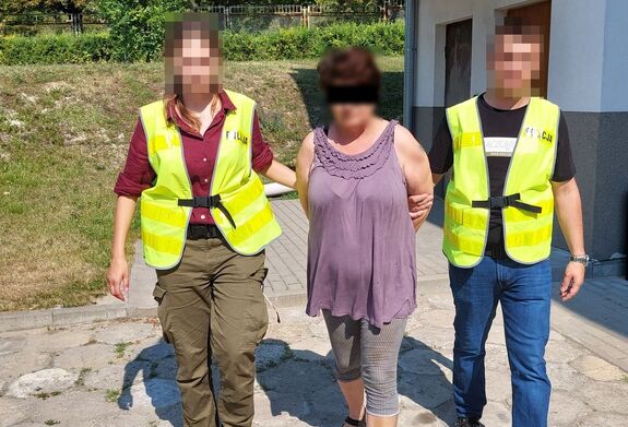 Policjanci prowadzą zatrzymaną kobietę.