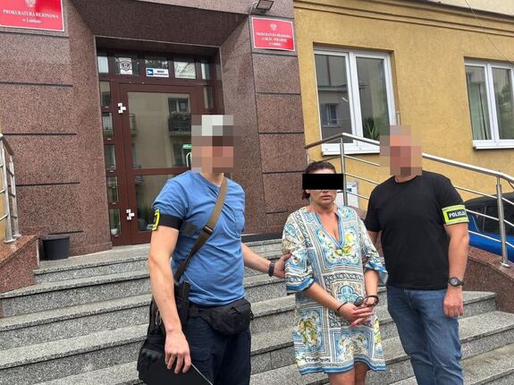 dwaj kryminalni prowadzą zatrzymaną oszustkę