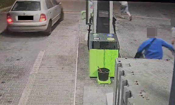 Pojazd na stacji paliw, po drugiej stronie biegnie 3 mężczyzn